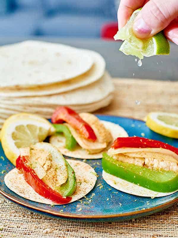 sizzling chicken fajitas on plate, lime squeezed overhead