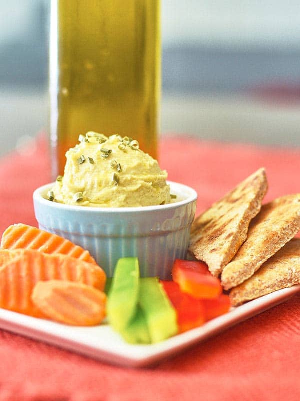 spicy jalapeno hummus in bowl on plate next to veggies and pita