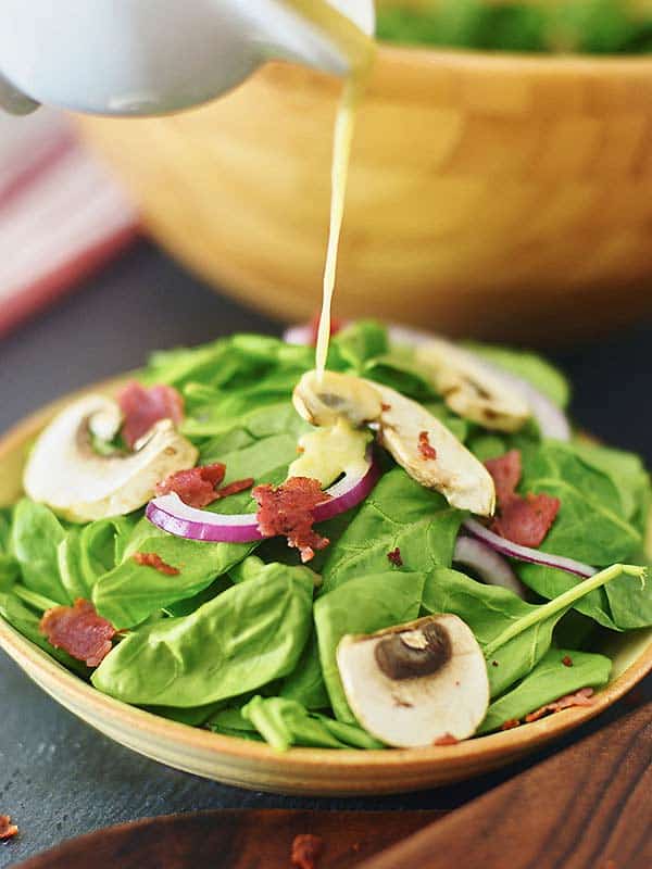 dressing being drizzled over plate of spinach salad