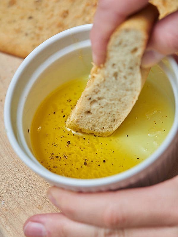 piece of parmesan herbed focaccia being dipped into bowl of olive oil