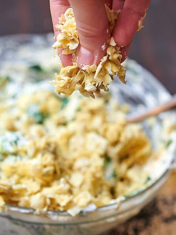 chopped artichoke hearts being sprinkled into bowl