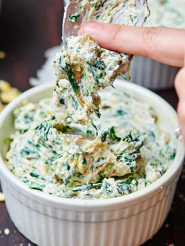 spoon being wiped off into bowl of spinach artichoke dip