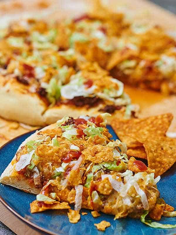 Slice of taco pizza on a plate, whole pizza in background