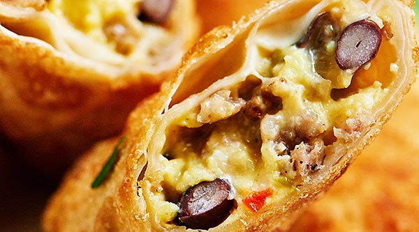 These breakfast egg rolls can be a fun change to your breakfast routine! The outside is perfectly crunchy and is filled with creamy eggs, gooey cheese, slightly crunchy veggies, salty sausage, and yummy black beans! It's hearty, it's delicious, and you're going to be hooked after one bite! showmetheyummy.com #eggrolls #breakfast #eggs #vegetables #sausage #fried