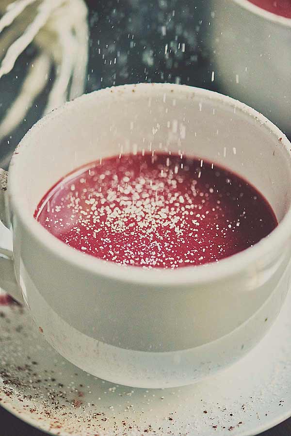 powdered sugar being sprinkled over mug of red velvet hot chocolate