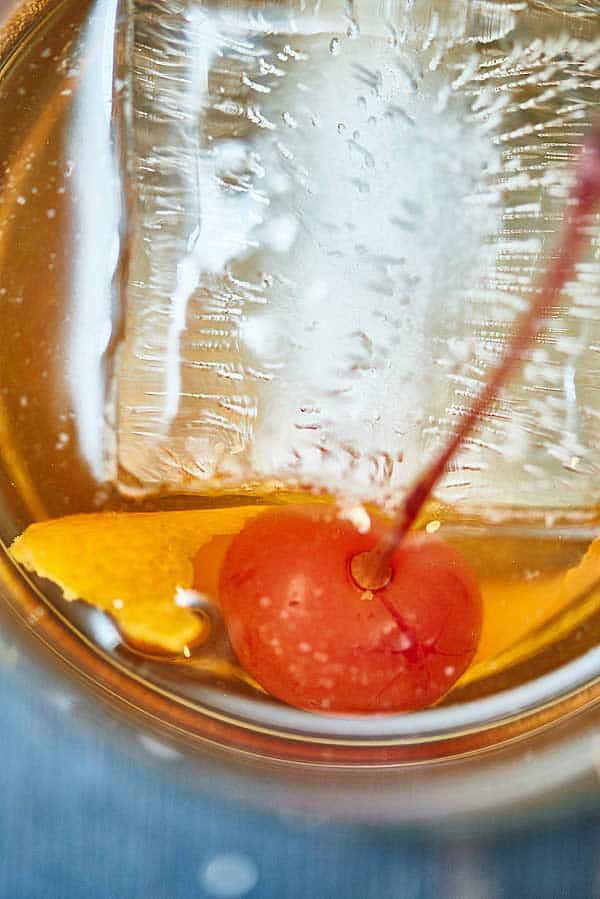 closeup of cocktail with ice cube and cherry above