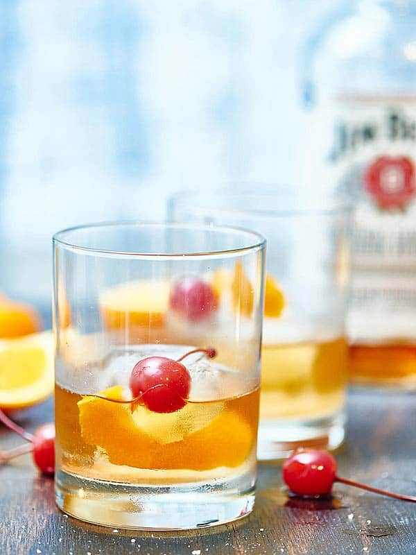 two old fashioned glasses with bottle of liquor in background