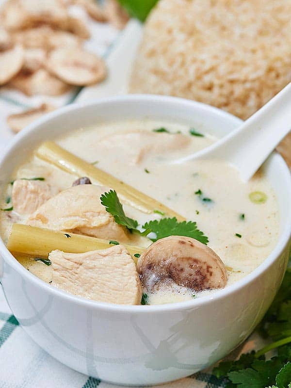 Bowl of tom kha gai soup from side with spoon highlighting mushroom, chicken, and cilantro