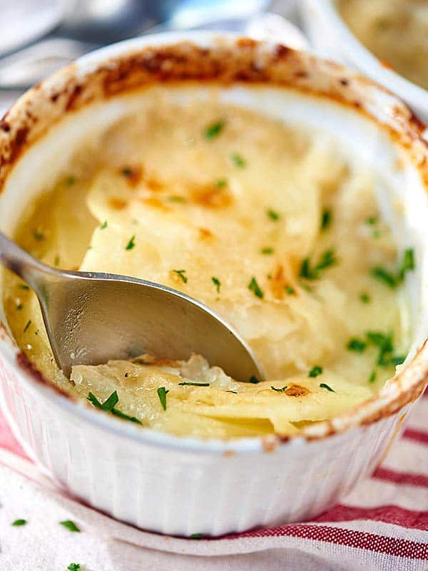 Bite being taken out of potato gratin bowl with spoon