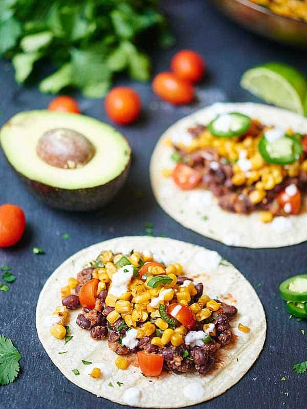 Two black bean and corn tacos next to half avocado