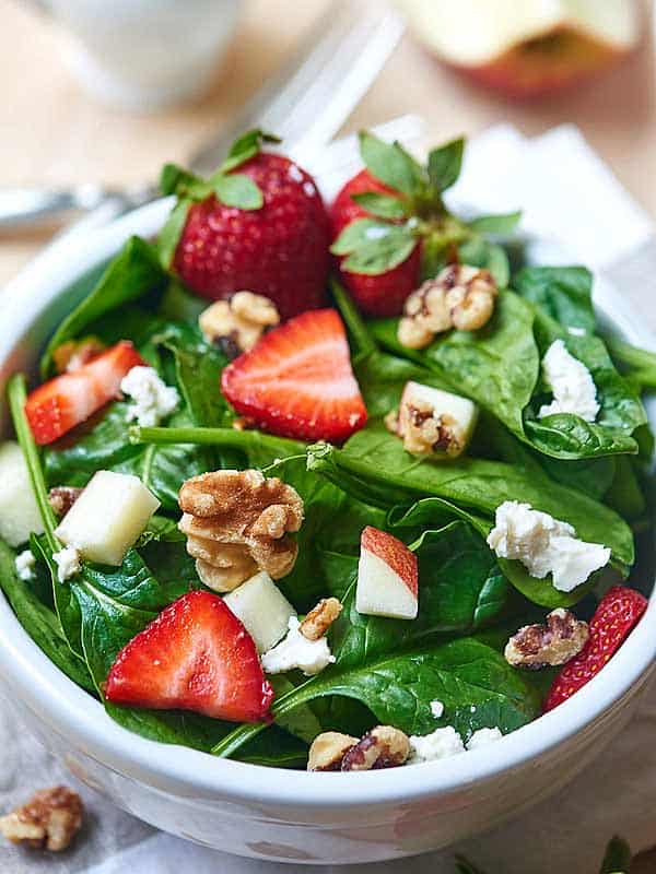 bowl of goat cheese spinach salad with strawberries above