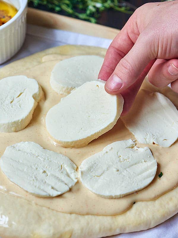 slices of mozzarella being put on pizza dough