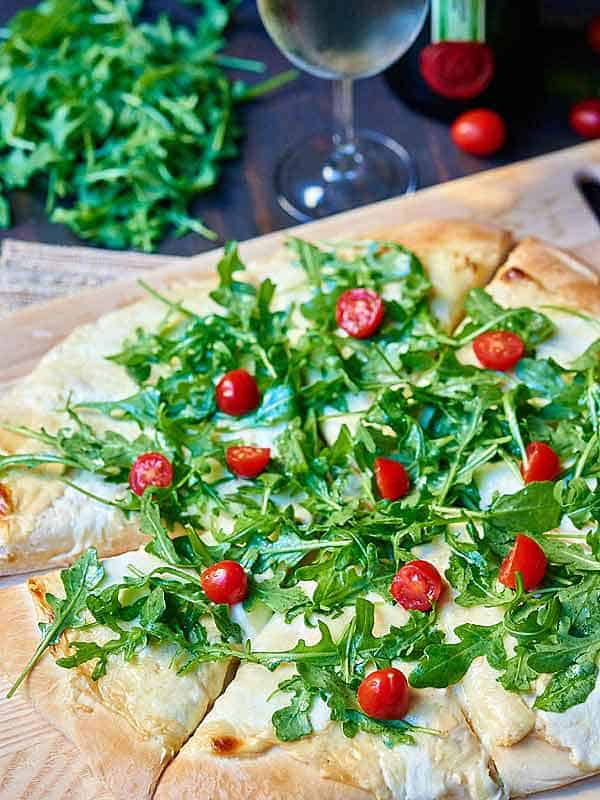 roasted garlic white cheese pizza with arugula on cutting board