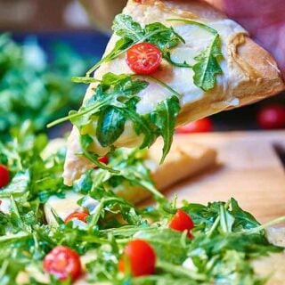 Once you’ve tasted this roasted garlic white cheese pizza with arugula salad you’ll never go back to store bought pizza again! Homemade crust is topped with a creamy, slightly spicy roasted garlic sauce, two types of cheese, and is baked to ooey gooey perfection! It’s then topped with a fresh arugula salad! Can we say perfection?! showmetheyummy.com #pizza #arugula #whitepizzasauce #whitepizza #cheese #vegetarian #garlic