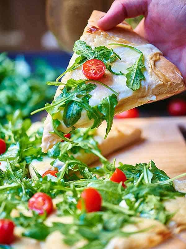 slice of roasted garlic white cheese pizza with arugula held