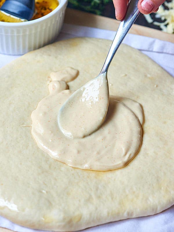 roasted garlic sauce being spread on pizza dough