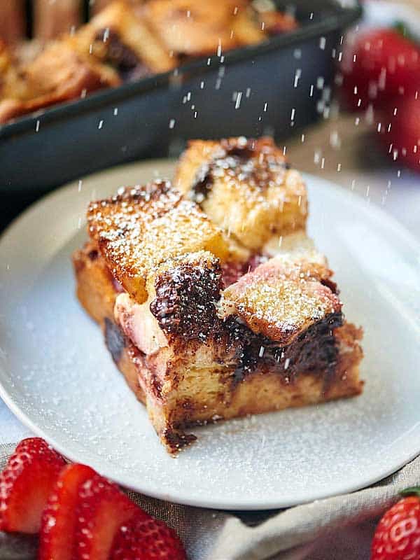 slice of french toast casserole on plate being sprinkled with powdered sugar