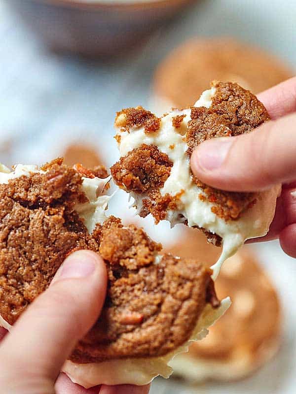 Carrot cake cookie sandwich with coconut cream cheese frosting being pulled apart