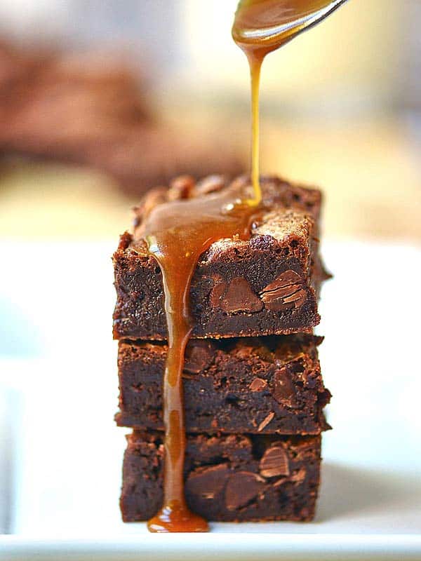 3 flourless salted caramel brownies stacked with caramel being drizzled on top