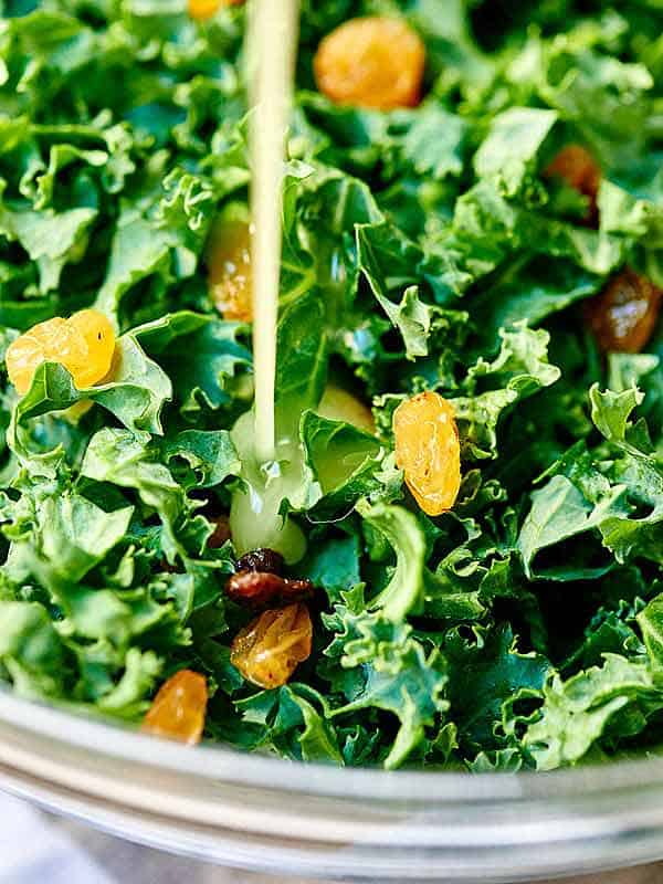 dressing being drizzled over bowl of kale salad