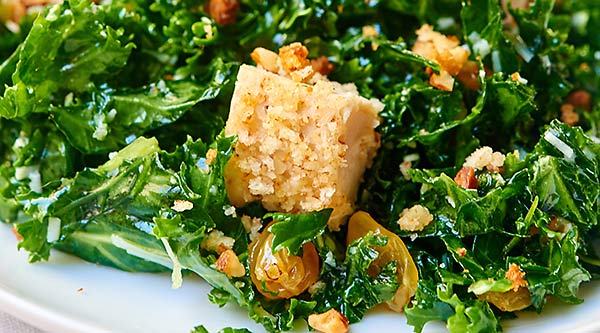 Kale Salad with Baked Almond Chicken. A healthy, protein packed salad full of massaged kale, pecorino romano cheese, golden raisins, almond chicken, and smothered in a fresh, lemony dressing! showmetheyummy.com #kale #salad #healthy #chicken #protein #lemon