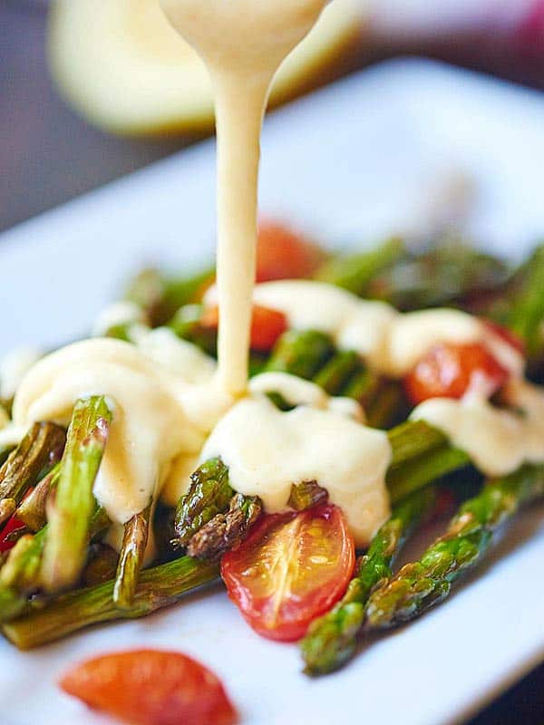lemon garlic hollandaise being drizzled on roasted asparagus and tomato