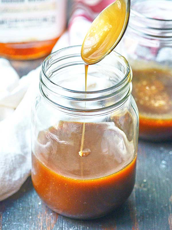 spoonful of caramel sauce being drizzled over jar of caramel sauce