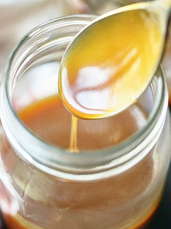 spoon being pulled out of jar of caramel sauce