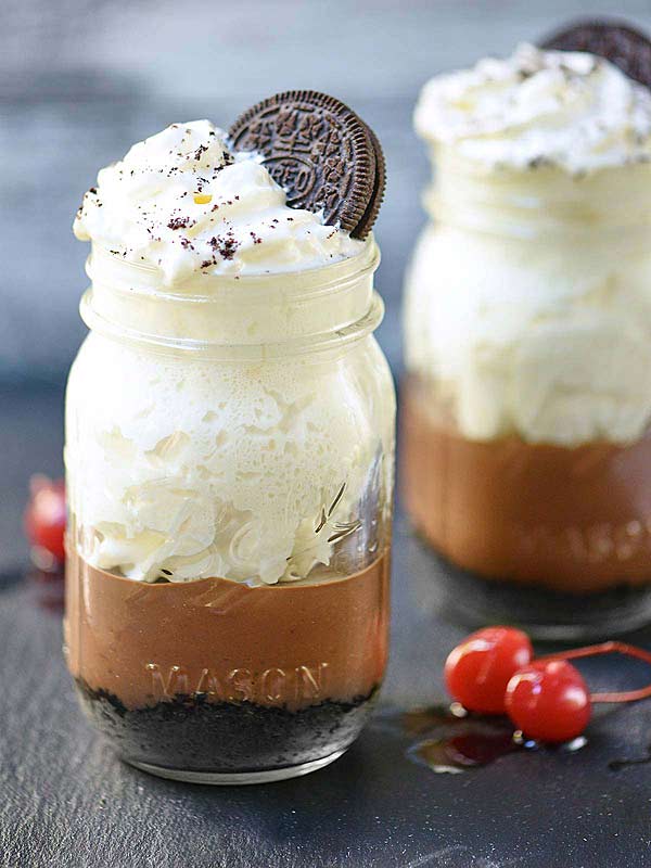 two mason jars of chocolate oreo pudding with whip and oreo cookie on top