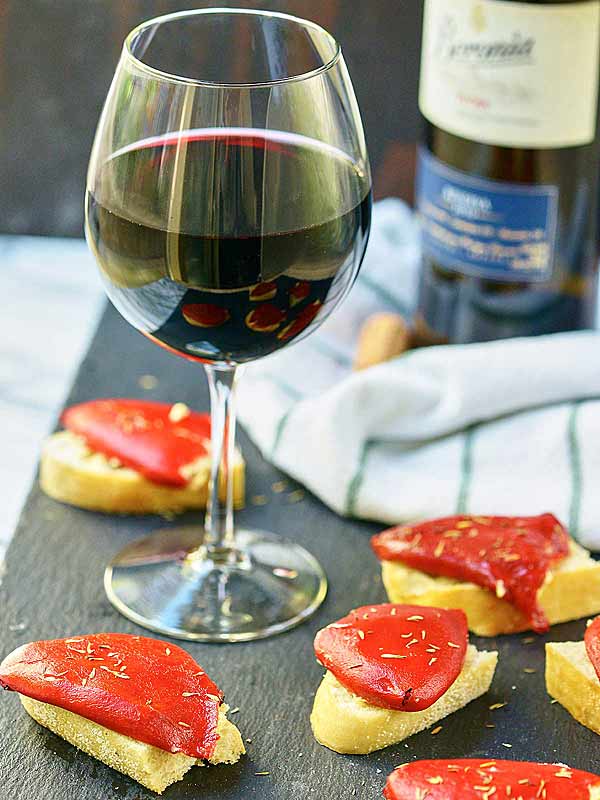 glass of wine next to piquillo peppers on bread