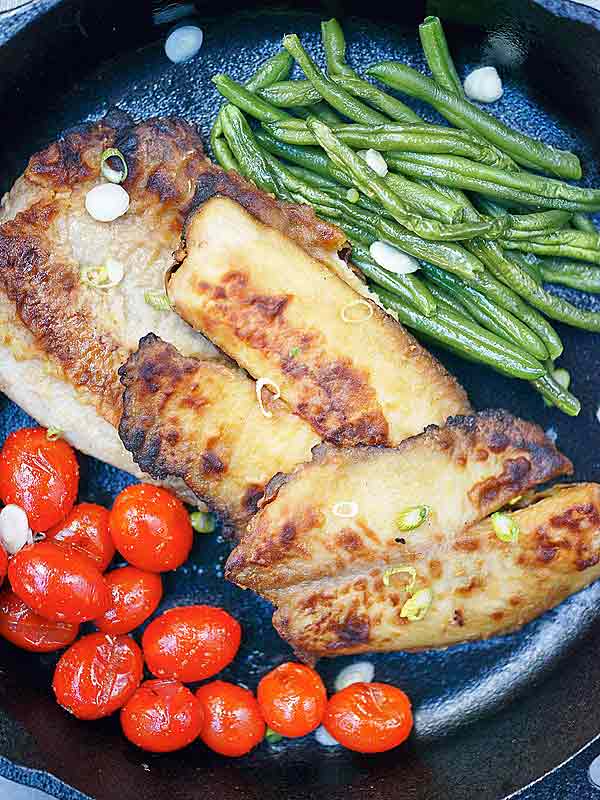 Garlic tilapia in skillet with veggies above