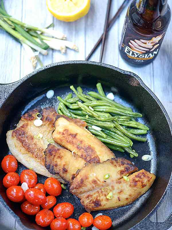 Garlic tilapia in skillet with cherry tomatoes and green beans above