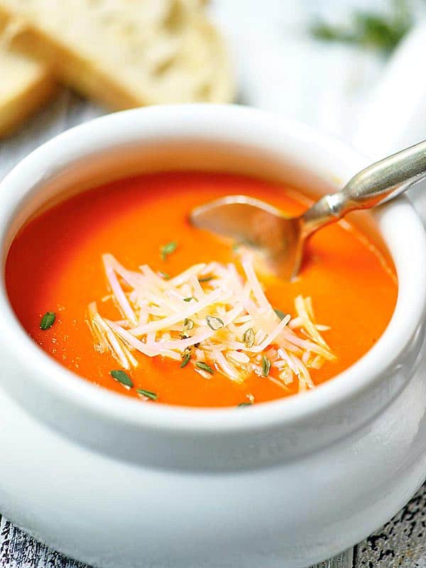 bowl of roasted red pepper soup with spoon and parmesan cheese