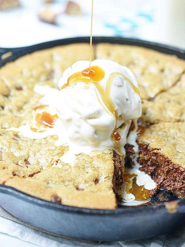 deep dish cookie in skillet with ice cream, caramel being drizzled on top