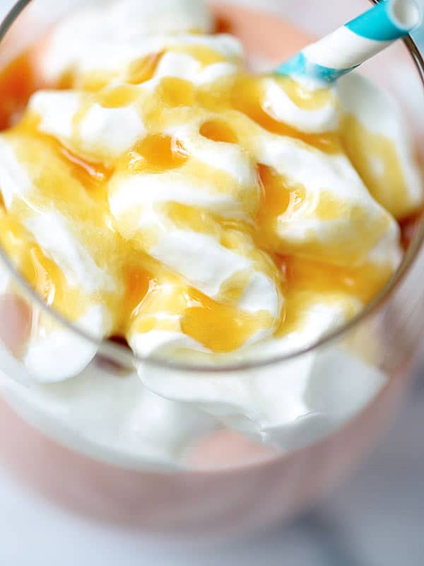 closeup of whipped cream and caramel drizzle on spiked tropical cake shake above
