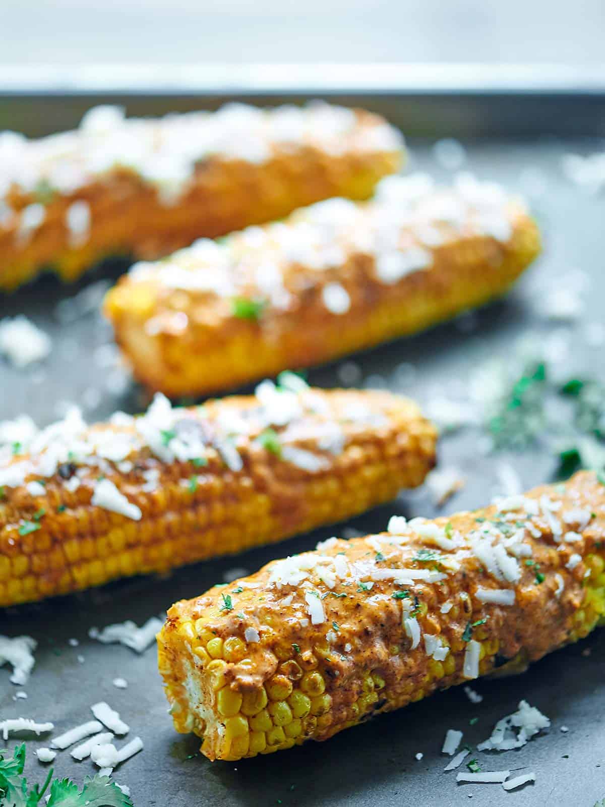 four cobs of mexican grilled corn on baking sheet