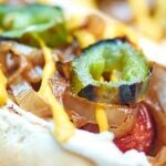 This Seattle hot dog recipe has turned me from a hot dog liker to a hot dog L.O.V.E.R. A lightly toasted hot dog bun piled with an all beef hot dog, slowly caramelized onions, smokey cream cheese, spicy jalapeños, and don't forget about those salty kettle chips for some crunch! showmetheyummy.com #hotdog #grilling #seattle #creamcheese #bacon #jalapenos #onions #chips