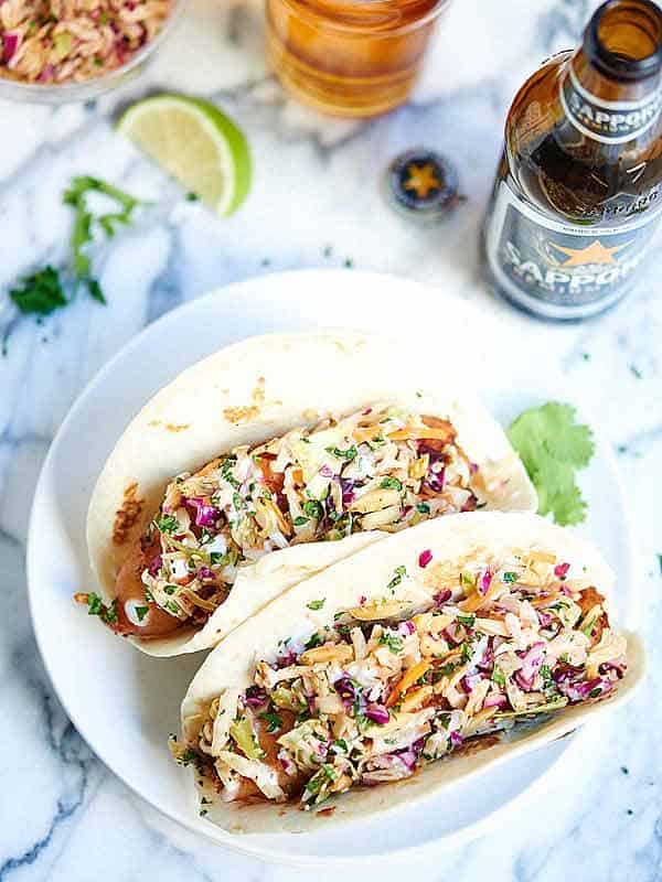 two fish tacos on plate next to bottle of beer overhead