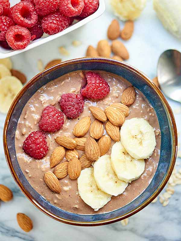 chocolate peanut butter jelly overnight oats in bowl with almonds, raspberries, and banana above