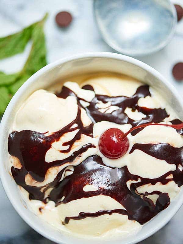 bowl of hot fudge sauce over ice cream with cherry above