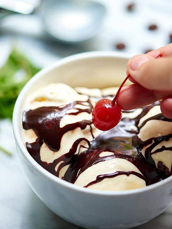 bowl of ice cream with hot fudge sauce, cherry being put on above