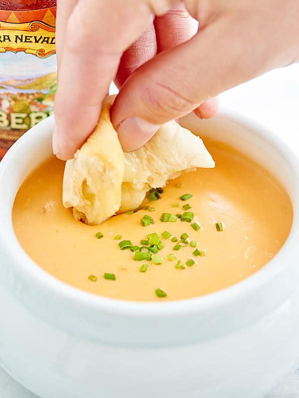 piece of biscuit being dipped into bowl of beer cheese dip