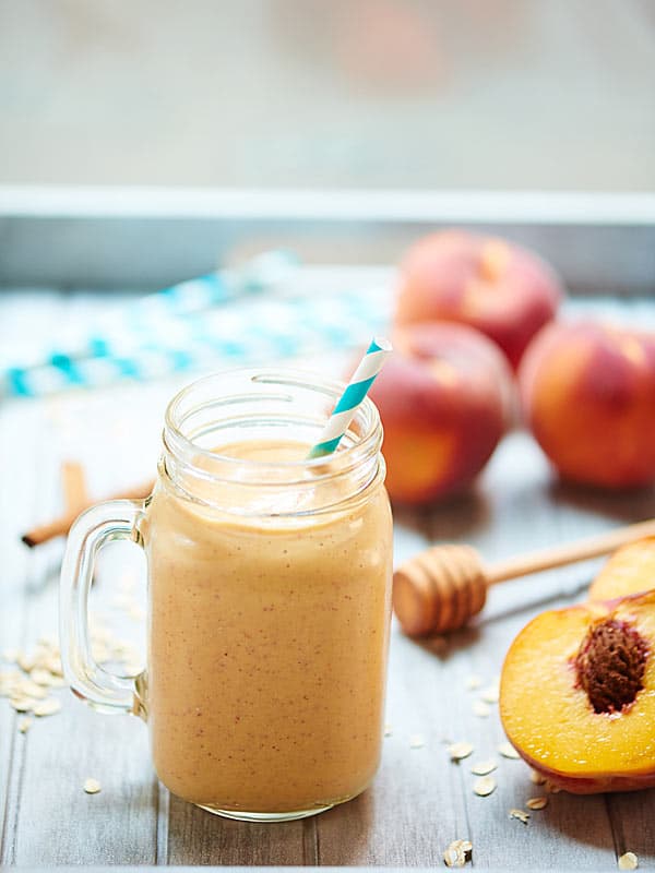 peach cobbler smoothie in jar next to halved peach