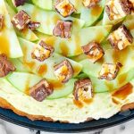 The BEST fall dessert: Snickers Caramel Apple Dessert Pizza. A giant peanut butter cookie topped with a fluffy caramel frosting, apples, and Snickers candy! showmetheyummy.com #snickers #caramel