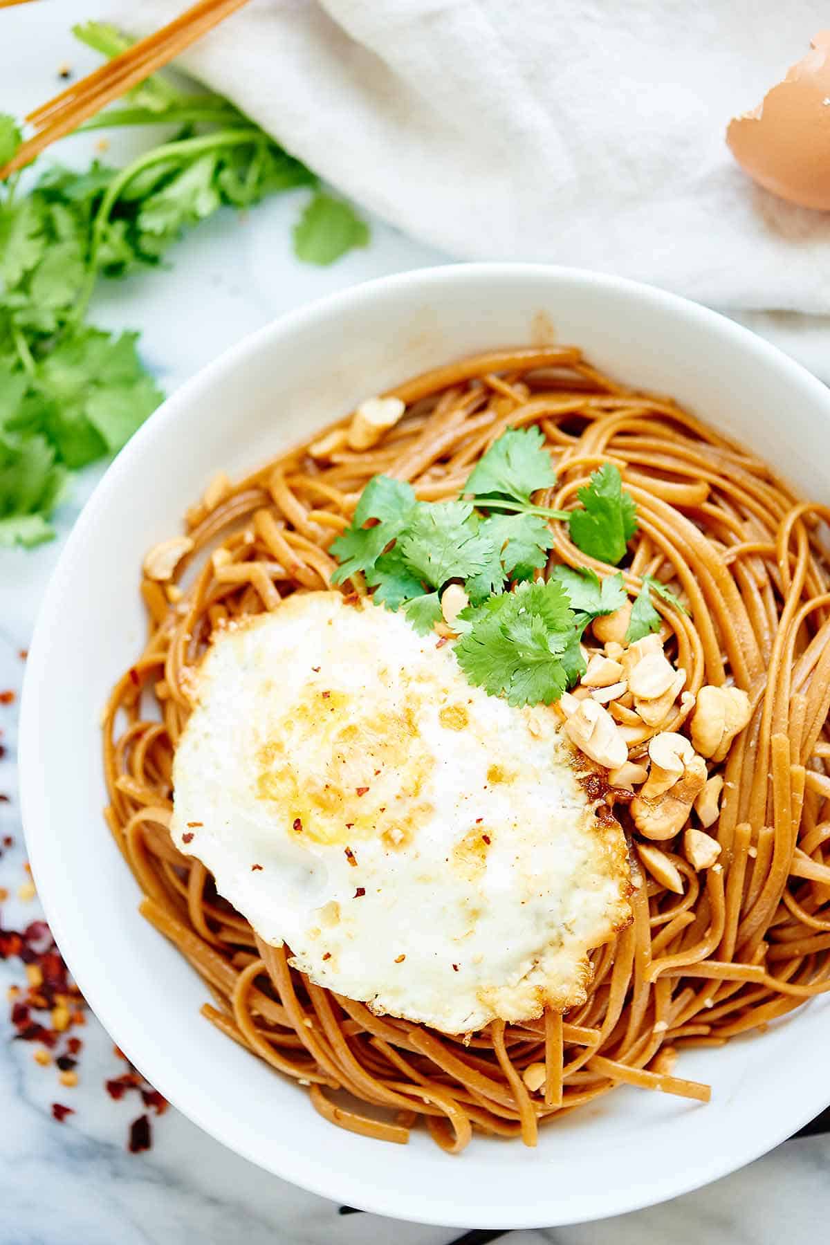 Asian noodles in bowl with fried egg and cilantro above