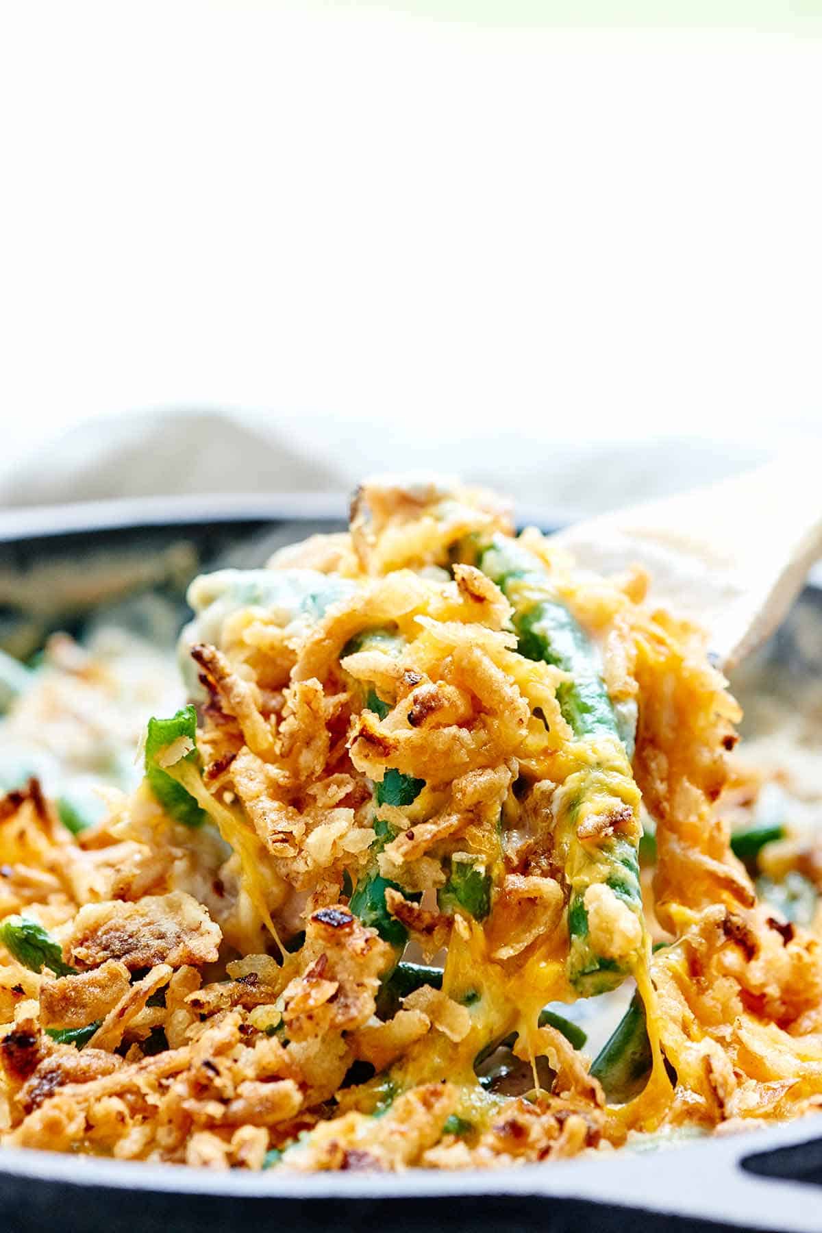 Green bean casserole scooped out of skillet with wooden spoon