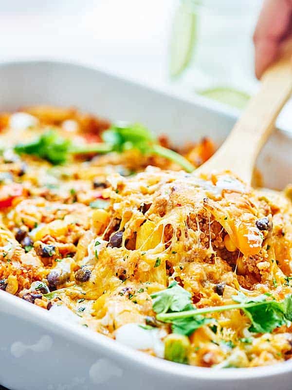 Casserole being scooped out of baking dish with wooden spoon