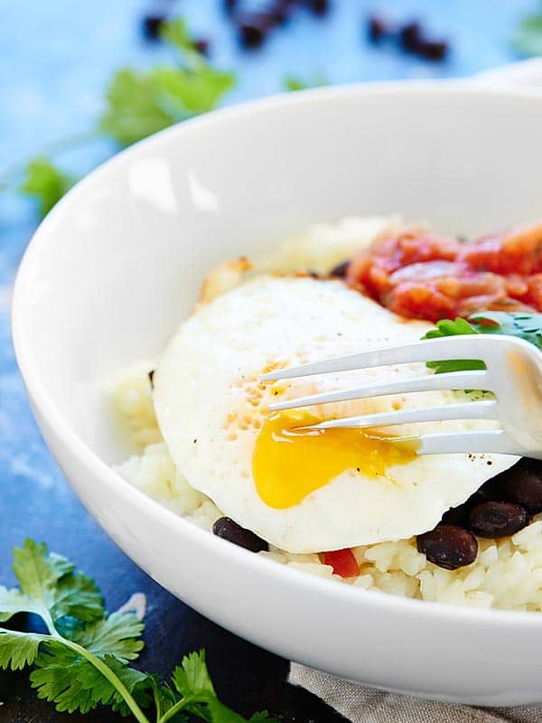 bowl of rice and beans with fried egg being cut with fork