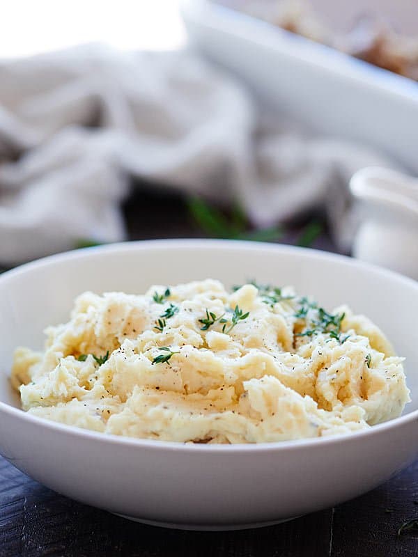 Side view of mashed potatoes in a bowl garnished with rosemary