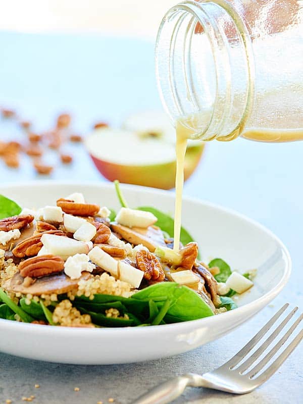 warm mushroom quinoa salad on plate being drizzled with dressing